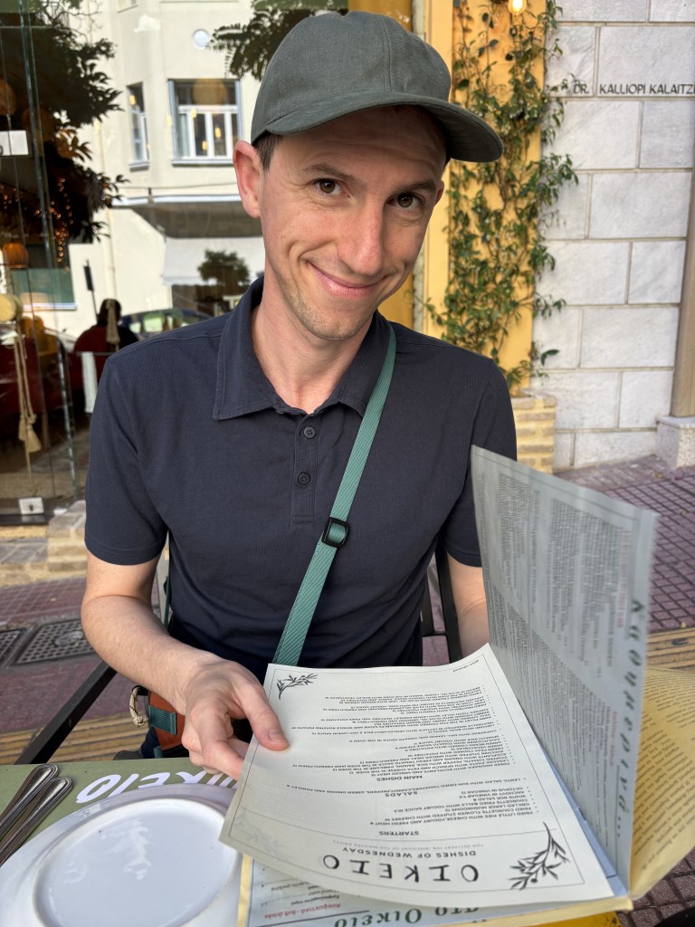 White male stilling at a restraint with a menu open in a blue shirt and a green hat